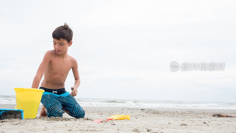 男孩准备在海滩上建沙堡