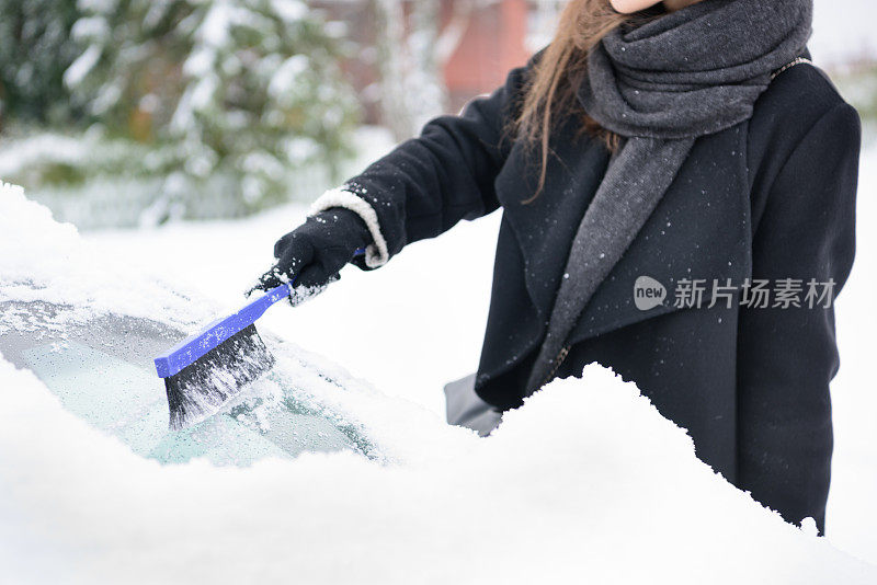 冬天即将来临。女人在冰冷的天气里，车被雪覆盖着。