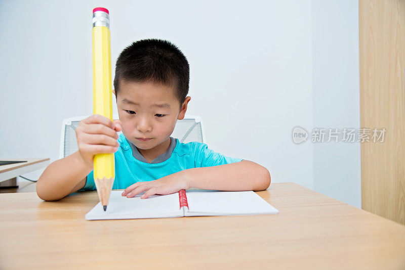 亚洲小男孩用一支大铅笔写字