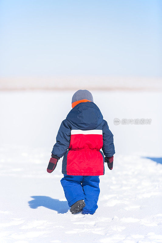 蹒跚学步的小男孩在雪地上行走的后视图