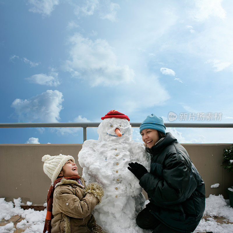 快乐的妈妈和女儿在阳台上玩雪人