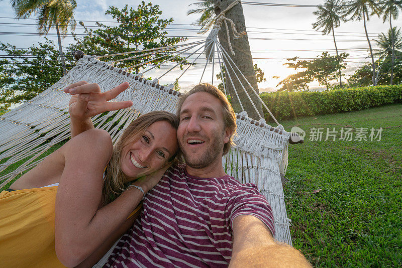 年轻夫妇在白色吊床上自拍，在热带气候下放松度假——人们在旅行中享受生活和自然，用移动设备技术捕捉凉爽的瞬间