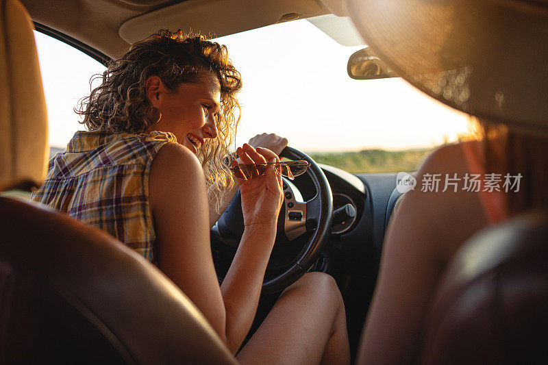 一个女孩坐在车里和她的朋友在一个阳光明媚的夏天开玩笑