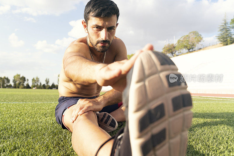 一个阳光明媚的日子，运动员在跑道上热身。一个男性运动员的肖像热身和伸展
