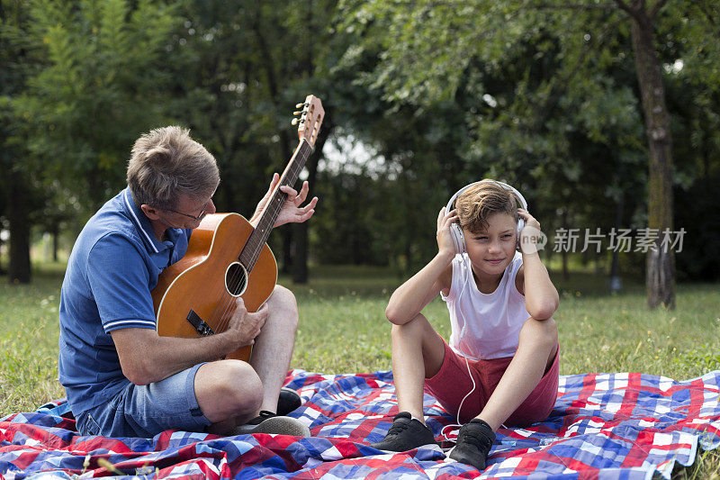 男孩戴着耳机听音乐，他的爷爷在弹吉他