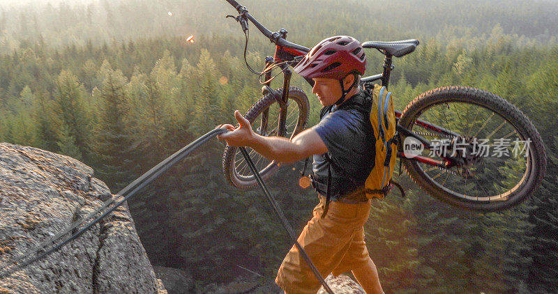 山地自行车手使用绳子爬山，在高山和山谷之上