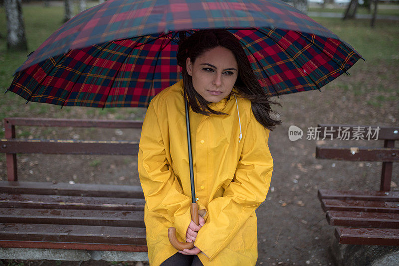 穿着黄色雨衣的年轻女子在公园里度过雨天