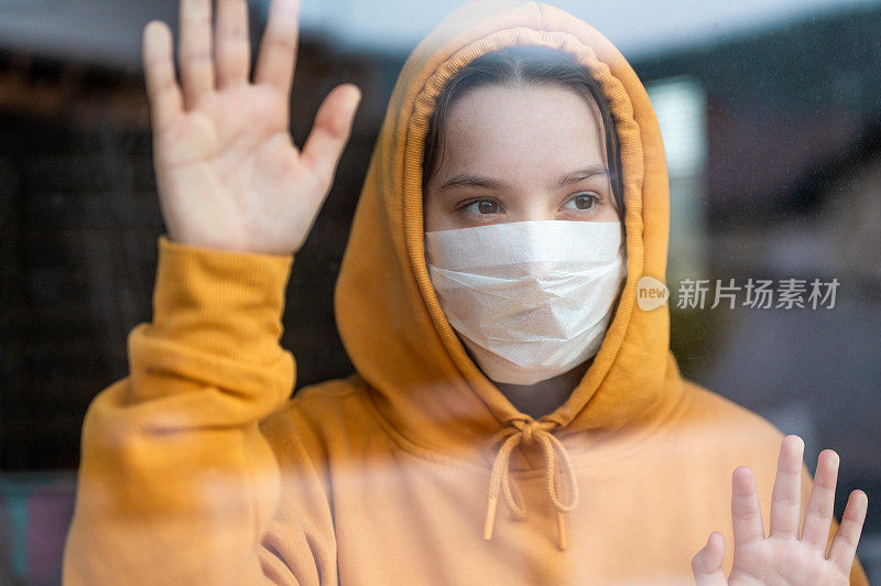 一个戴着外科口罩的少女站在窗前看