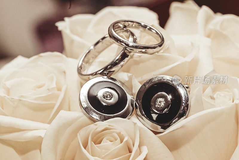 两个结婚戒指和两个奶油色玫瑰的新郎袖扣