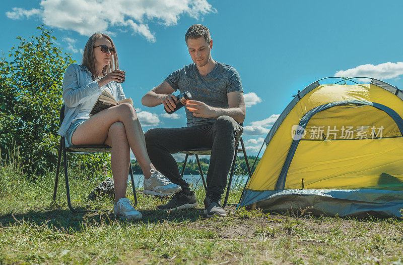 在湖边露营帐篷附近，女人和男人用保温瓶喝茶。