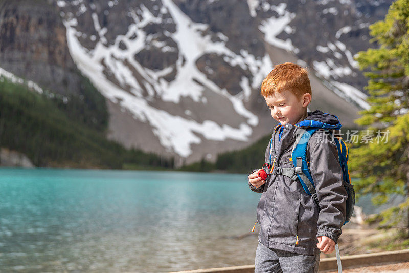 快乐年轻可爱的红发男孩走在小径在冰碛湖在夏天