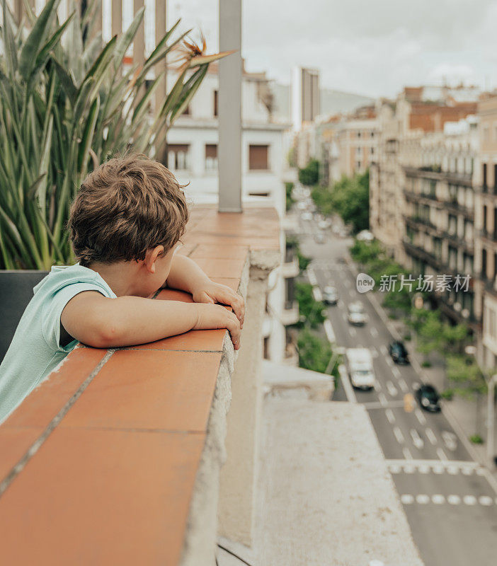 一名男孩在接受COVID-19隔离期间从阳台上看着街道