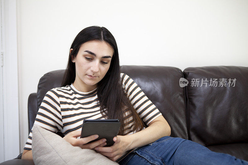 一名年轻女子在沙发上使用电子阅读器