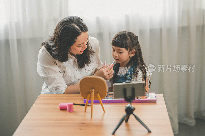 快乐年轻的亚洲母亲和她的女儿录制视频博客在家里与化妆主题