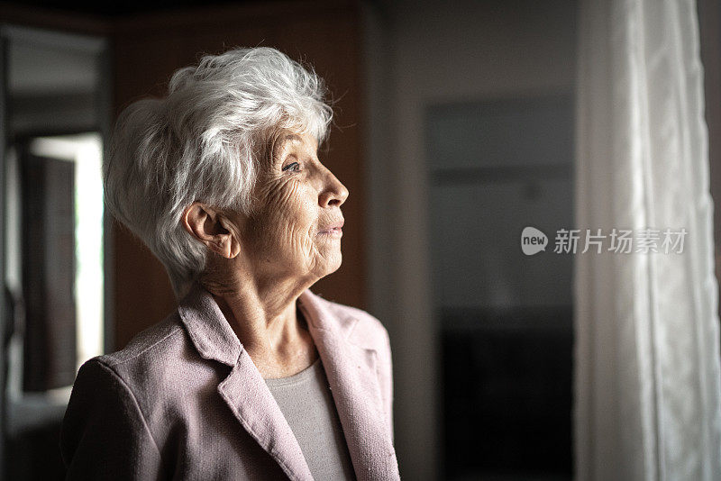 一位忧心忡忡的老女人透过窗户看着窗外，想着
