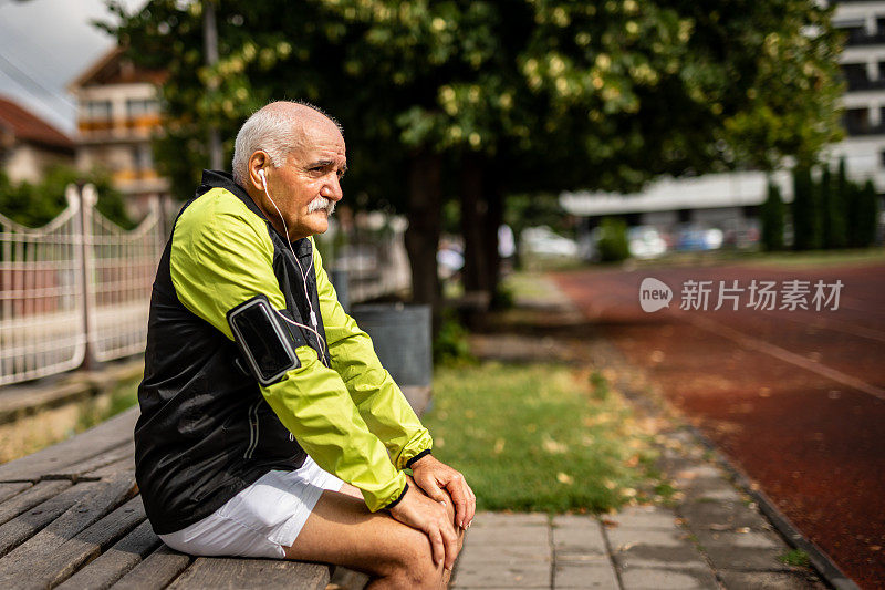 一个活跃的老人坐在跑道旁边的长椅上