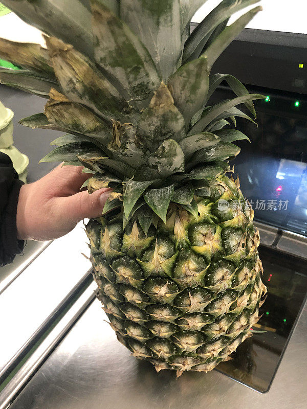 在超市自助结账处，一个不知名的人拿着菠萝进行扫描(自助结账)