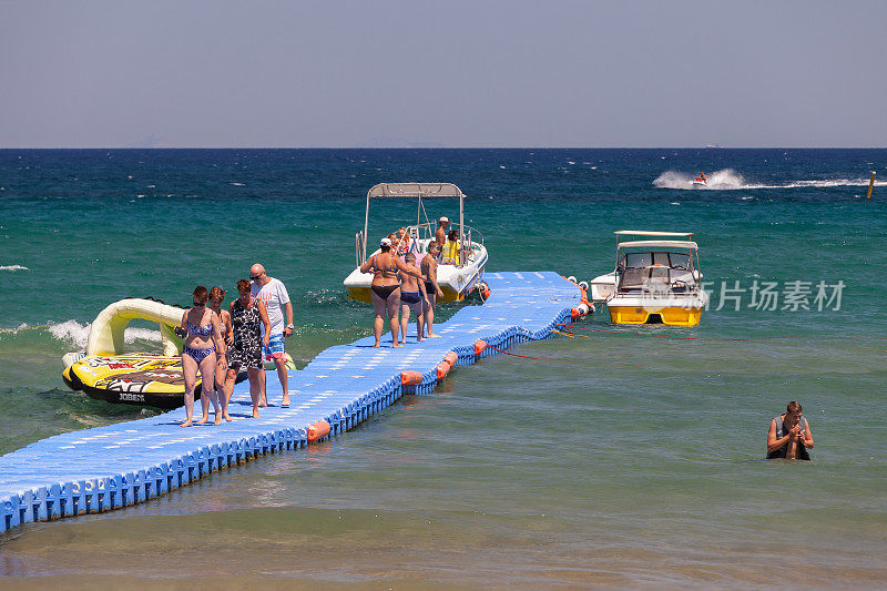 在希腊，游客们走在一个蓝色的塑料漂浮码头上