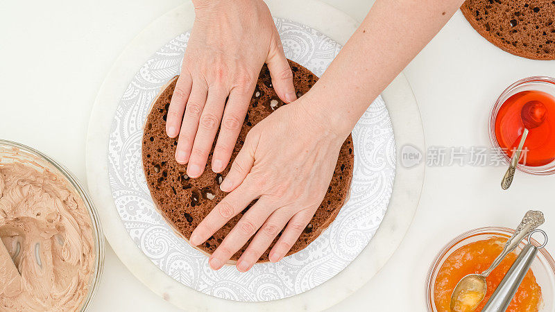 巧克力蛋糕用奶油和巧克力釉一步一步制作。女人双手组装蛋糕，平放着