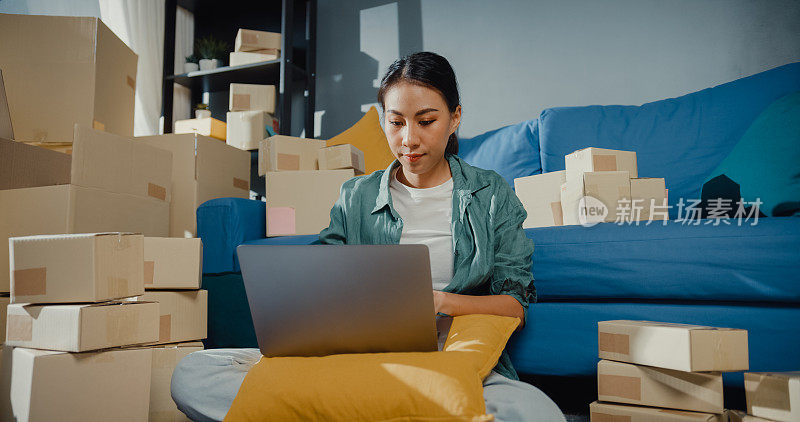 年轻的亚洲女售货员在网上商店使用笔记本电脑准备包裹，以装运到客户在家里。
