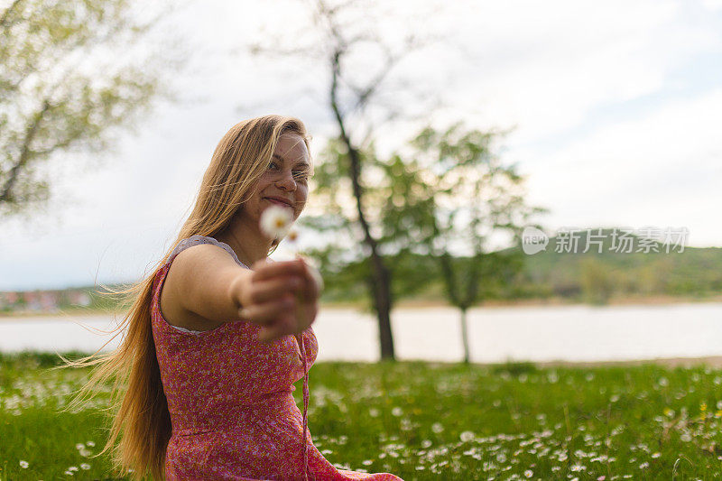 一个小女孩坐在湖边，穿着太阳裙，手里拿着一朵花