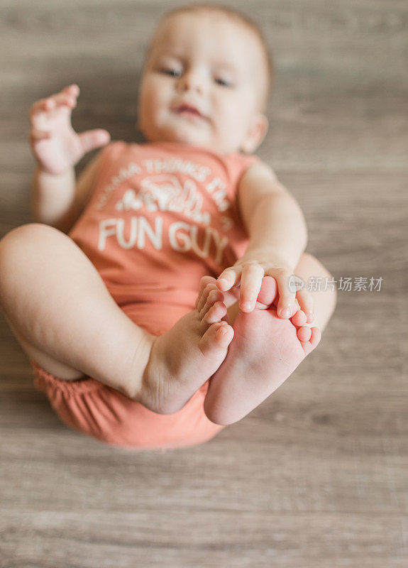 7个月大的男婴有12个脚趾，穿着一件珊瑚色的紧身衣，上面写着“妈妈认为我是一个有趣的人”，上面画着蘑菇菌类