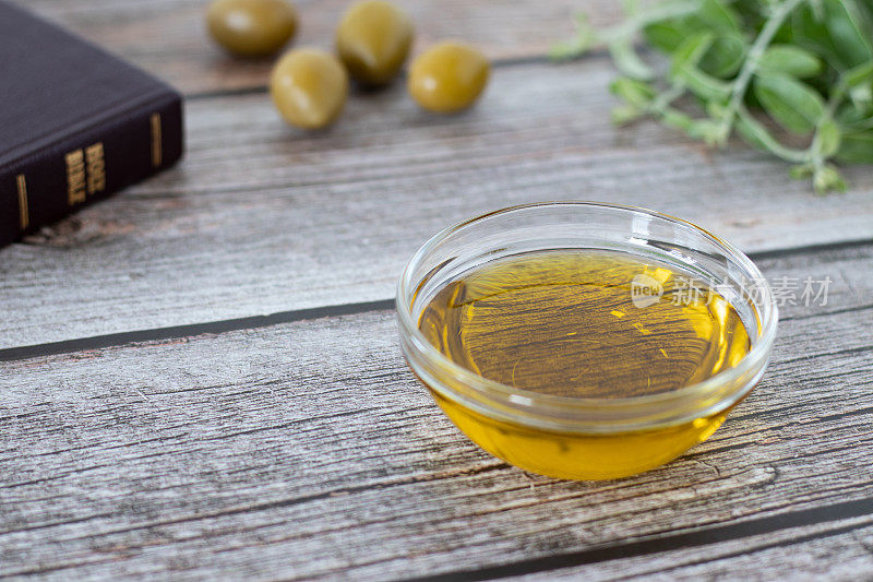 特级初榨橄榄油装在玻璃容器里，夹一本合上的圣经书，绿色的橄榄枝，放在木桌上