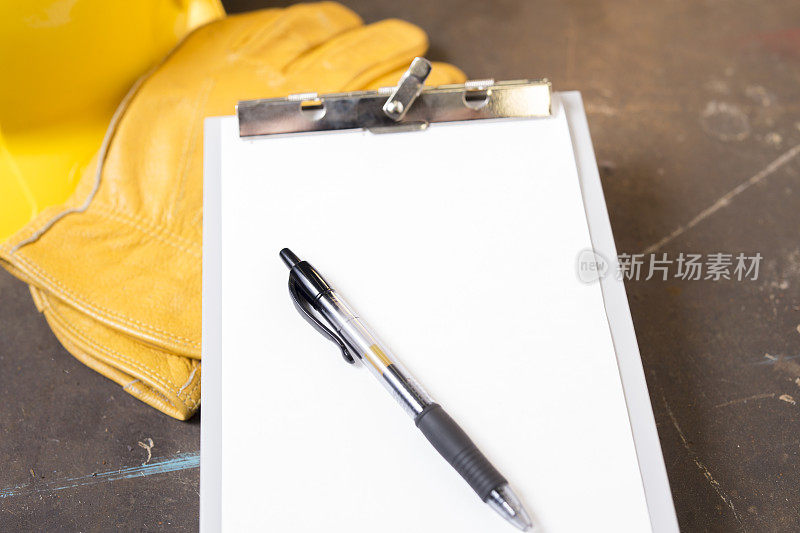 蓝领黄色安全帽和手套放在木桌上，白纸和一支笔。