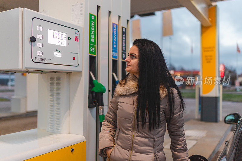 一名沮丧的年轻女子在加油站给她的柴油车加油时看着价格