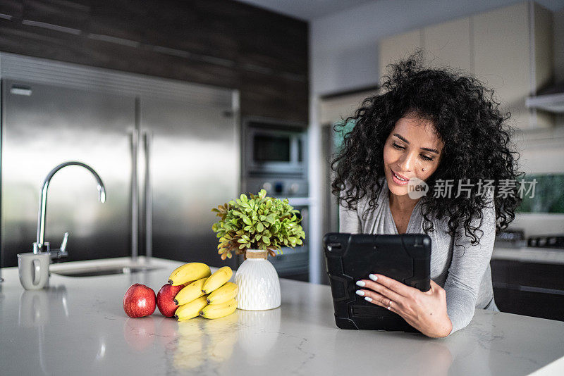中年妇女在家里的厨房里使用数码平板电脑