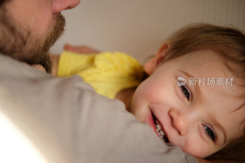 快乐的父亲和女儿，小女孩。一岁的宝宝笑着，笑着，抬头看着爸爸。男人向孩子示爱。坦诚的真实情感。胡子爸爸和小孩。真实的家庭生活方式。