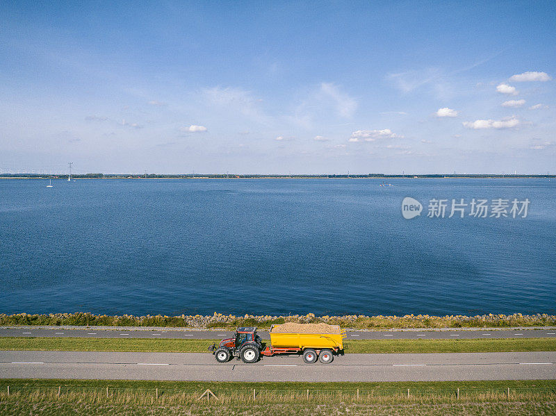 牵引拖车的拖拉机行驶在湖边的乡村道路上