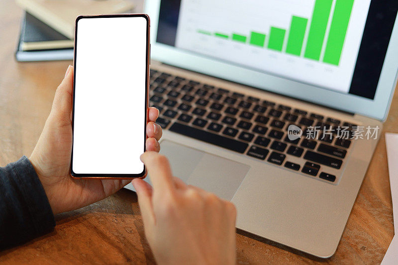 一个女人拿着空白屏幕的智能手机，用笔记本电脑做财务计划和预算。