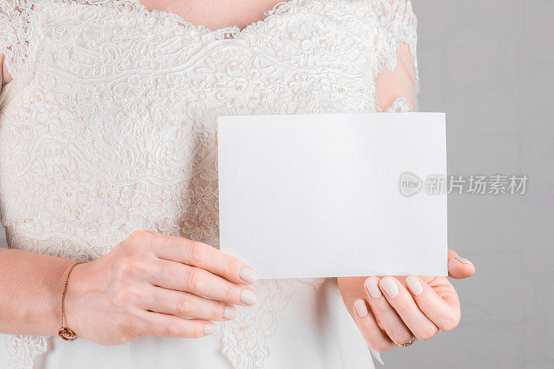 身穿婚纱的女子手持白色墙壁背景上7x5的婚礼舞台邀请卡模型