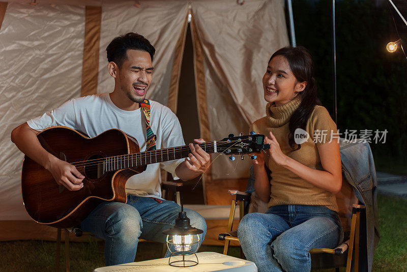 一对亚洲夫妇在野外露营度假旅行时，一边弹吉他一边唱歌。