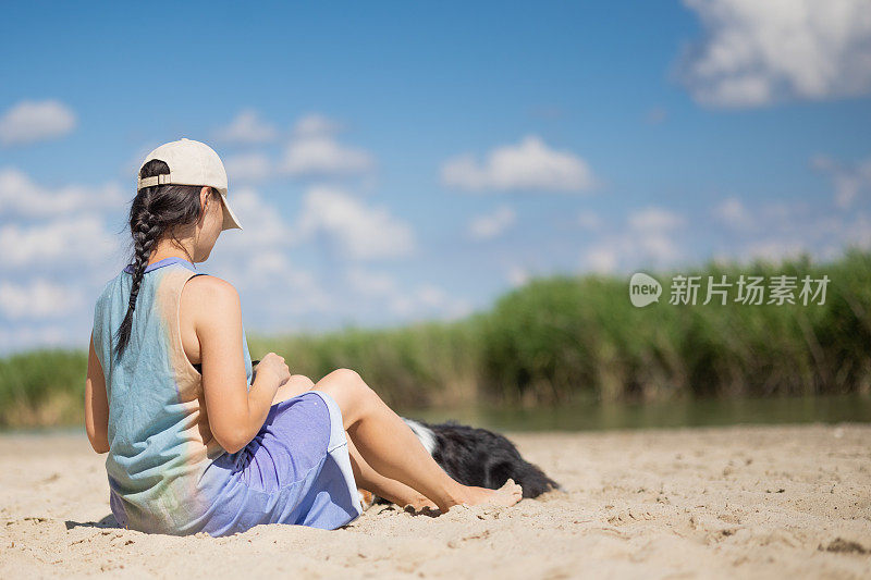 年轻女子带着狗坐在沙滩上