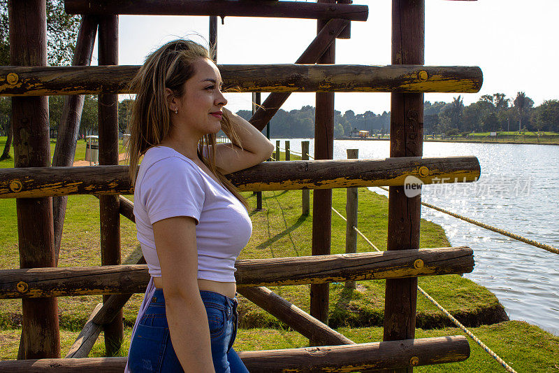 美丽的年轻女子站在湖边的木楼梯旁，看着远处