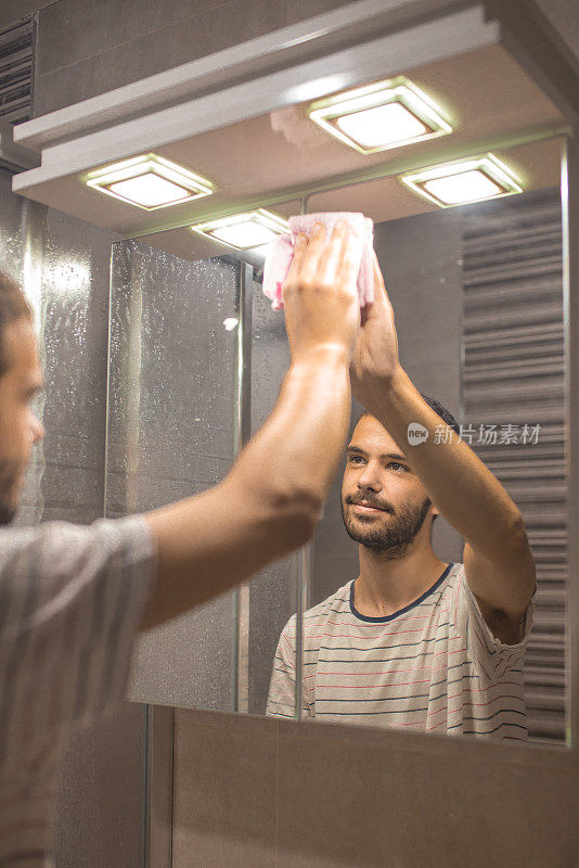 年轻人用清洁巾擦拭浴室镜子
