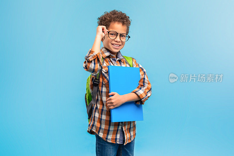 微笑的学生穿着格子呢衣服，调整着眼镜，拿着蓝色文件夹