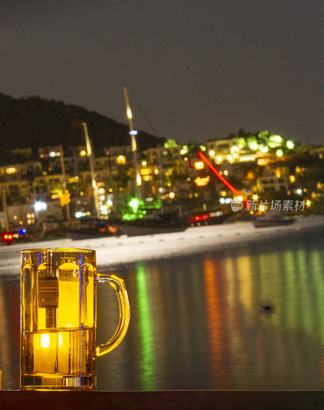 在酒吧的桌子上喝啤酒，晚上欣赏美丽的海景