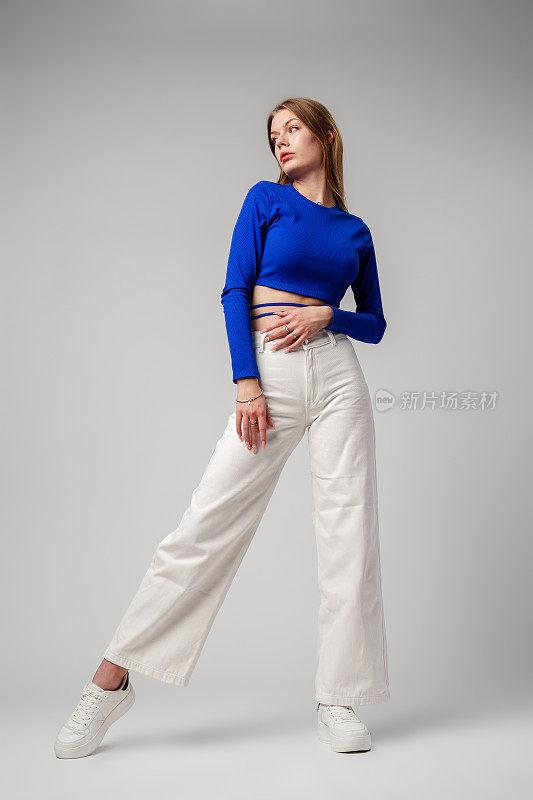 年轻女子模特在蓝色上衣和白色裤子摆姿势在白色背景