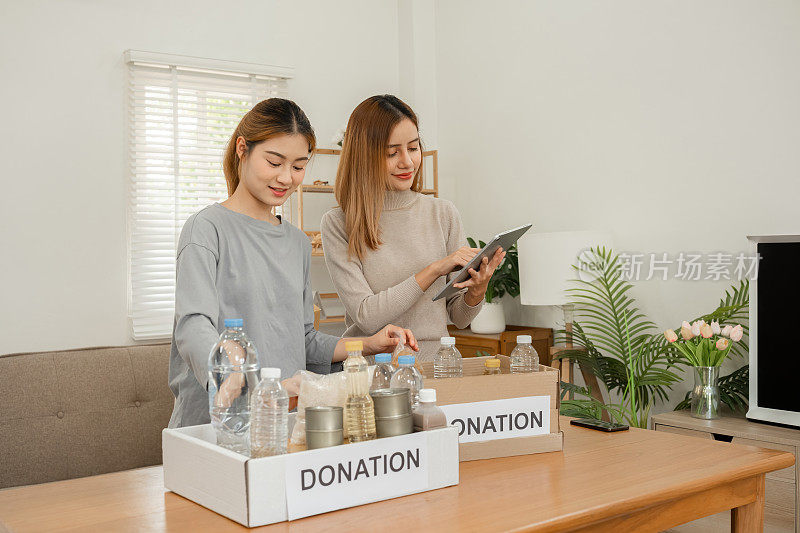 两名年轻的女志愿者帮助把食物装进捐款箱，并准备把捐款箱送到慈善机构。