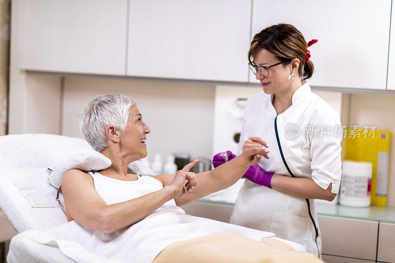 一位老年妇女躺在美容中心，正在接受一位女性技术员的糖化脱毛手术