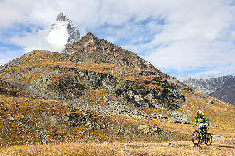 年轻的山地自行车手穿过马特洪山下面的山地草地