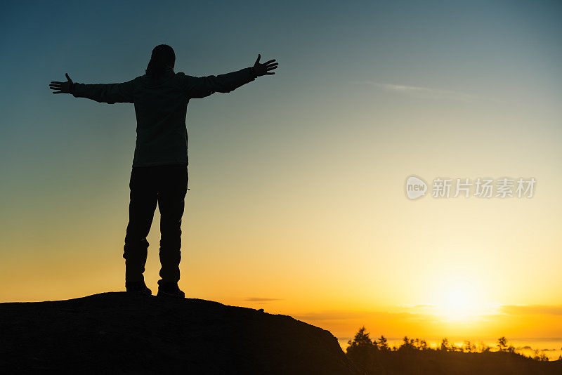 日落时分，山顶上一个女人伸出双臂的剪影