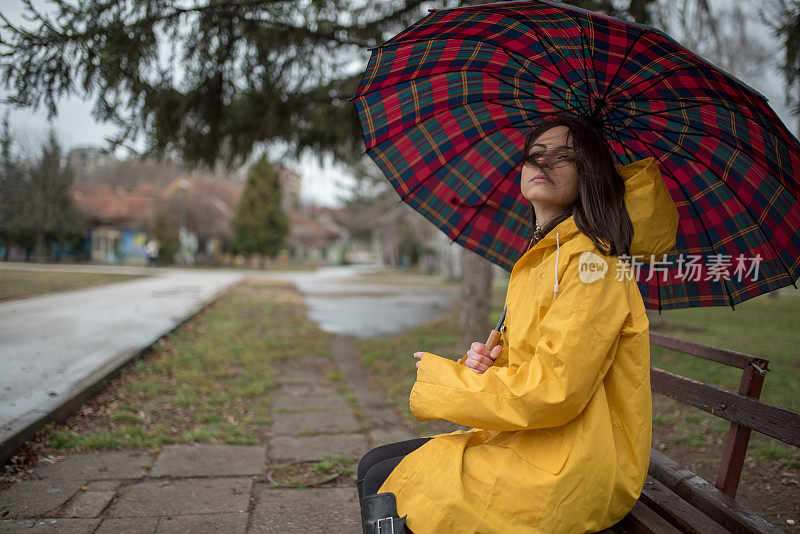 穿着黄色雨衣的年轻女子在公园里度过雨天