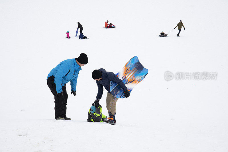 两名男子帮助小孩爬上雪橇山