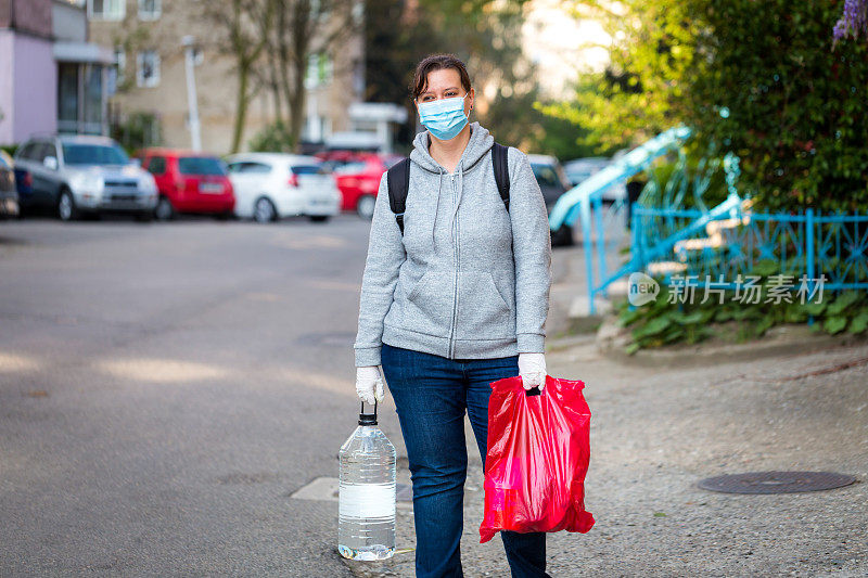 妇女戴着防护面罩和手套在户外搬运杂货