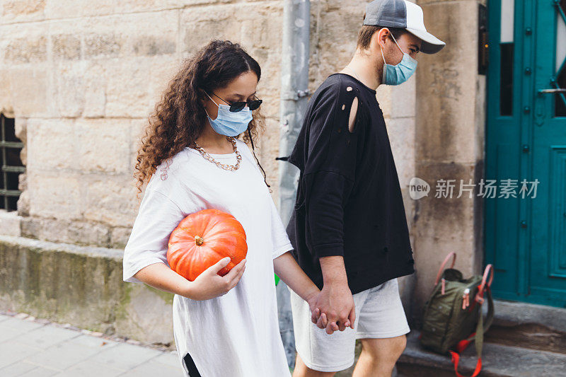 一名年轻女子和一名戴着防护面具的男子学生在秋天的周末带着南瓜走在老街上