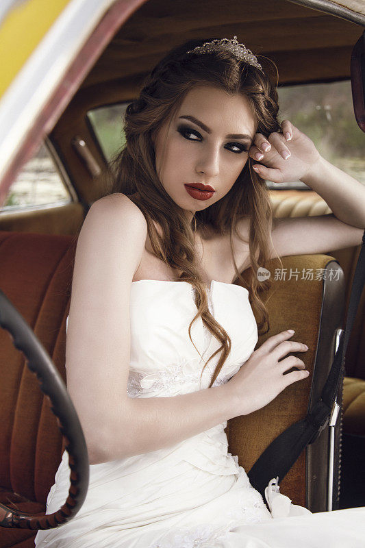漂亮的年轻新娘坐在经典车里。